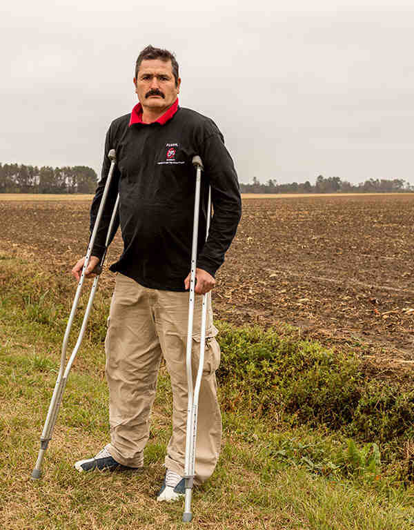 Arturo Hernandez stands on crutches in a field in North Carolina.