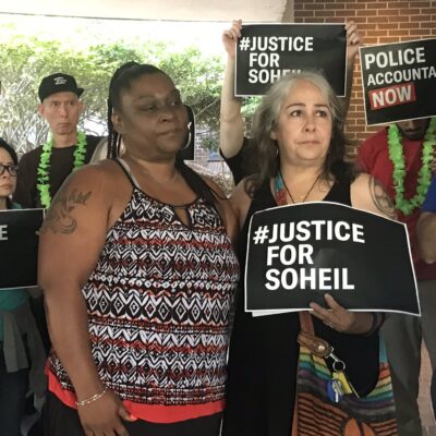 The mother of Soheil Antonio Mojarrad holds a "Justice for Soheil" sign at a PACT rally