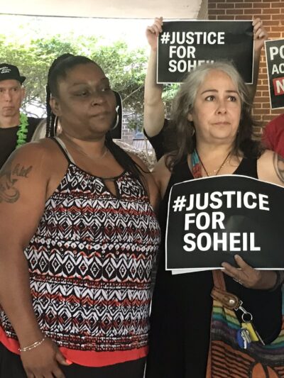 The mother of Soheil Antonio Mojarrad holds a "Justice for Soheil" sign at a PACT rally
