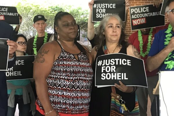 The mother of Soheil Antonio Mojarrad holds a "Justice for Soheil" sign at a PACT rally