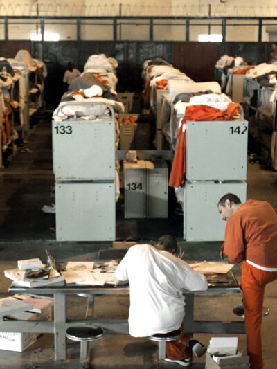 Incarcerated people lying in rows of prison bunk beds.