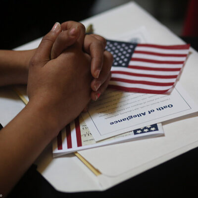 A participant folds her hands of a copy of the Oath of Allegiance and an American flag while listening to speeches during a naturalization ceremony