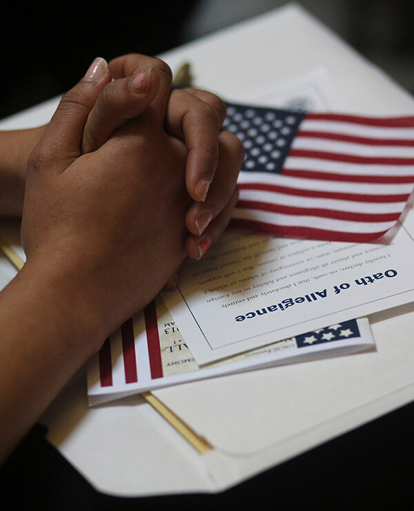A participant folds her hands of a copy of the Oath of Allegiance and an American flag while listening to speeches during a naturalization ceremony