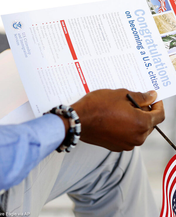 The hand of a seated person holding a miniature U.S. flag and immigration information at a naturalization ceremony.
