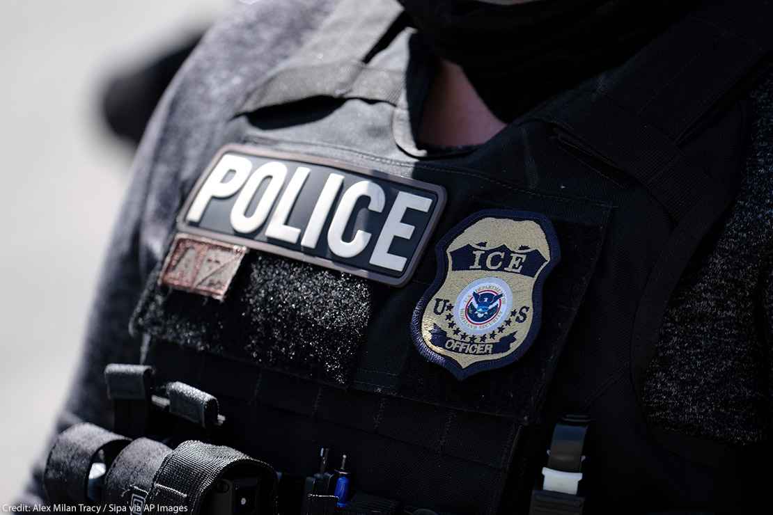 A close up of a police officer wears a "Police" label beside a U.S. ICE (standing for Immigration and Customs Enforcement) badge on his vest.