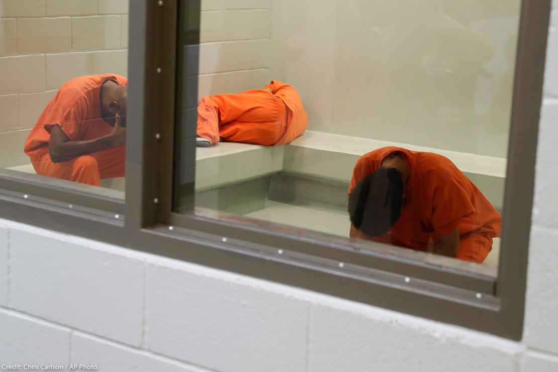 Three detainees waiting together inside a room to be processed at a detention facility.