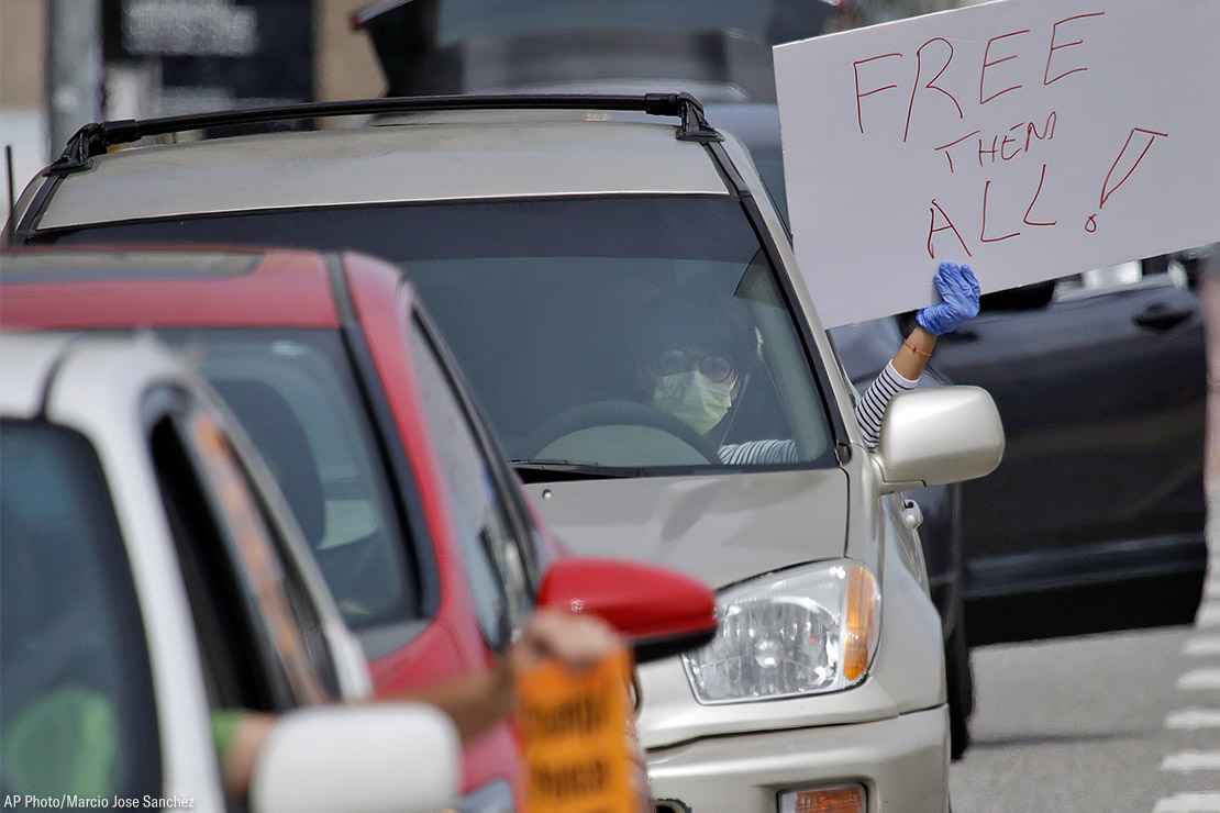 A demonstrator holds a sign with the text "Free Them All" in a car-based protest to demand the release of immigrants in California detention centers over COVID-19 concerns.