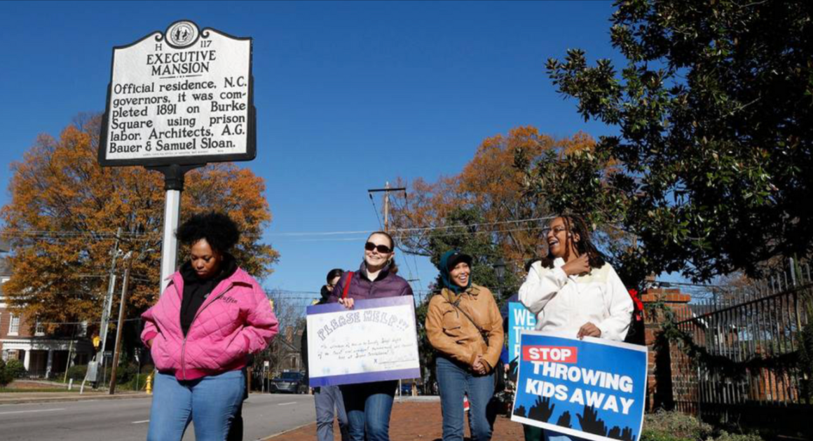 A group of protesters walk past the Governor's Mansion historical marker.