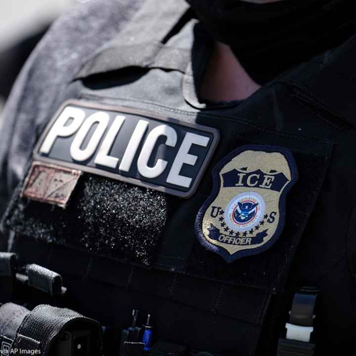 A close up of a police officer wears a "Police" label beside a U.S. ICE (standing for Immigration and Customs Enforcement) badge on his vest.