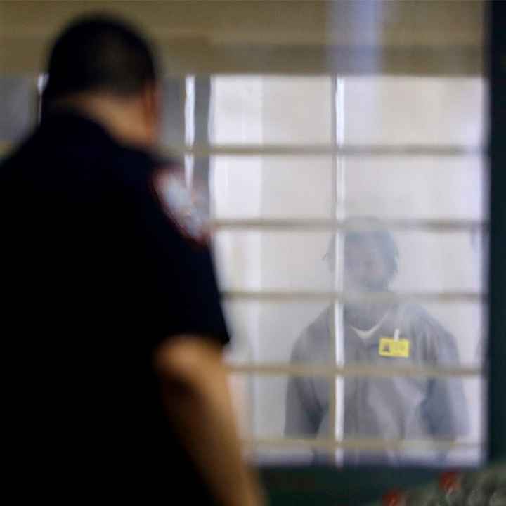 An incarcerated prison looking at a corrections officer separated by bars and a thick plastic barrier.