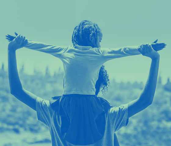 Child sitting on parent's shoulders with arms outstretched.